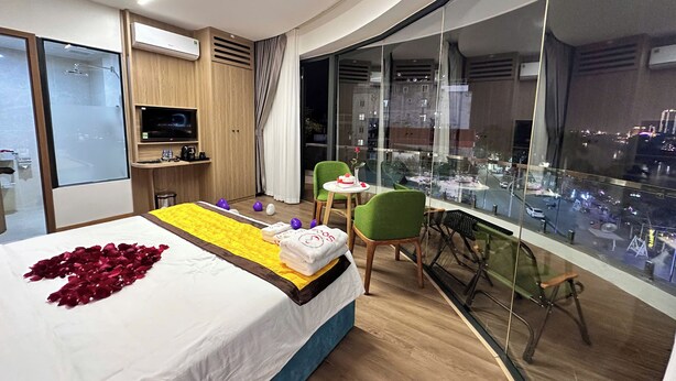 A hotel room with a bed, a small desk, a TV, and a balcony with a city view. - SOCA HOTEL LAO CAI (Lao Cai)