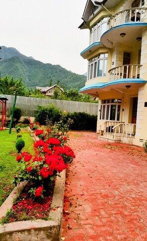 Un edificio con balcón, un jardín de flores rojas y montañas al fondo.