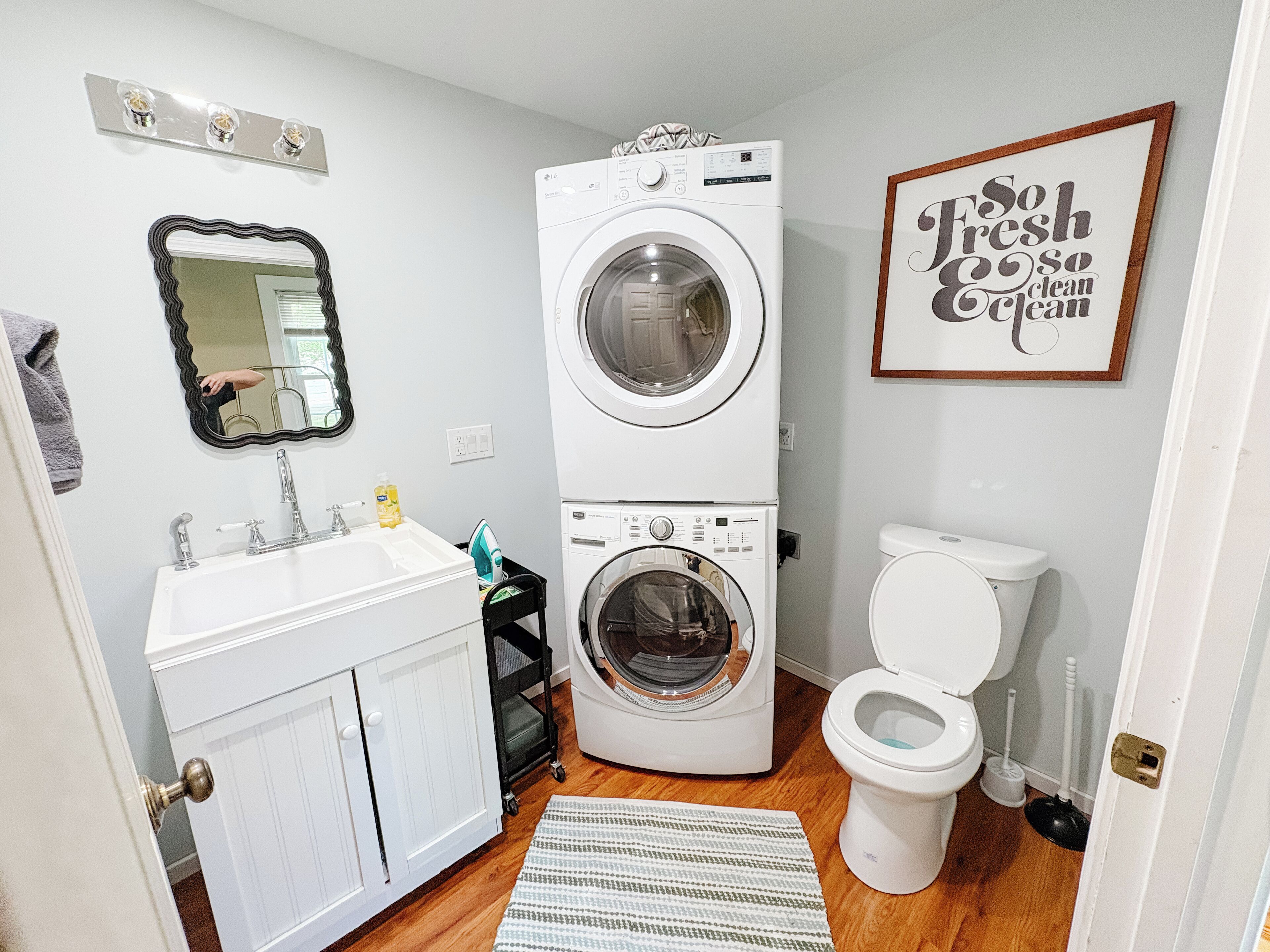 A compact bathroom with a double washer and dryer, a sink, a toilet, and a mirror.
