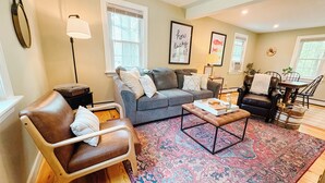 A cozy living room with a leather armchair, a grey sofa, a coffee table, and a patterned rug.