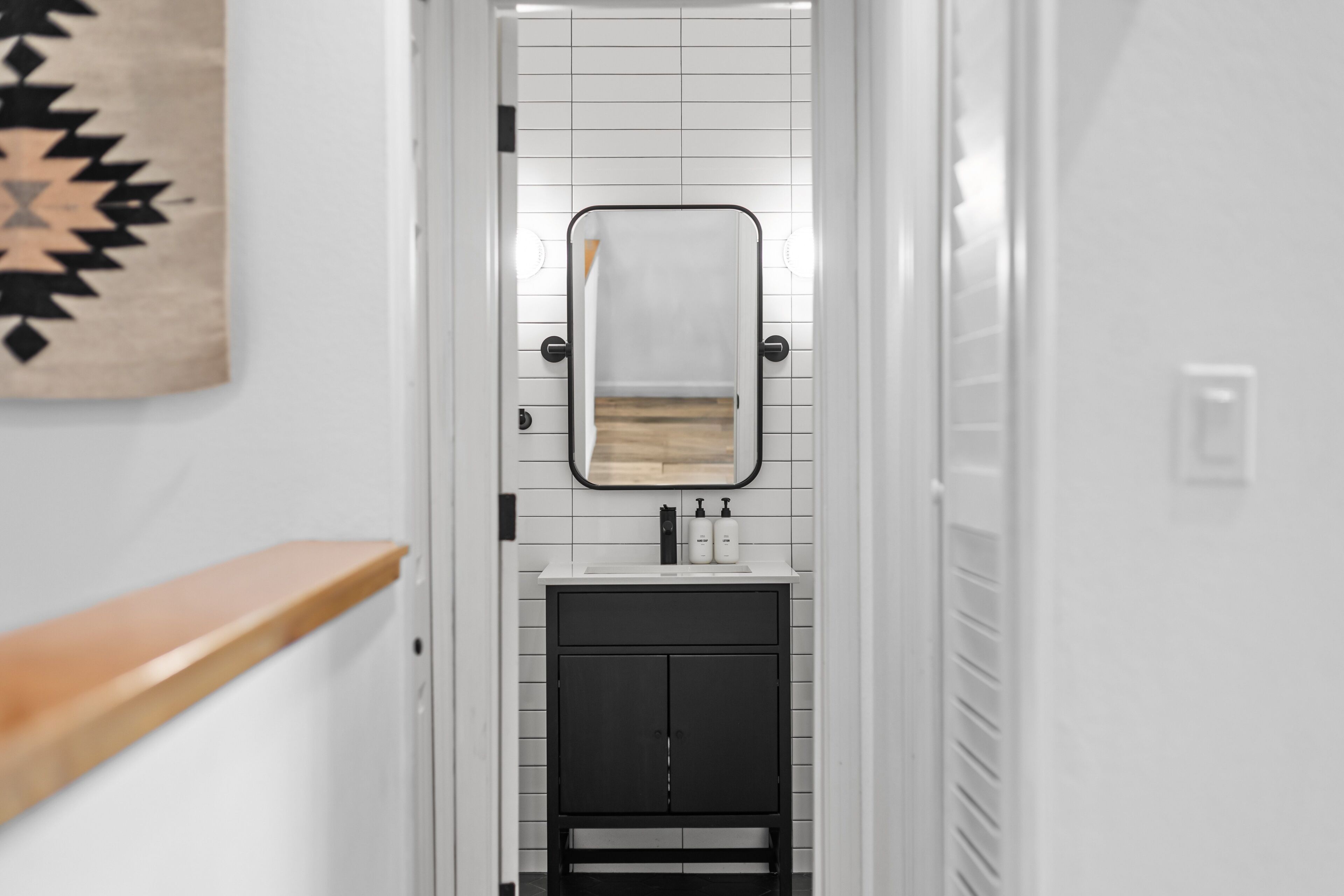 A narrow hallway leading to a bathroom with a white tiled wall, a black cabinet, and a wooden counter.