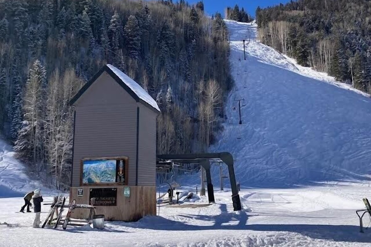 A ski lodge with a wooden exterior, a ticket window, and a ski lift in the background.