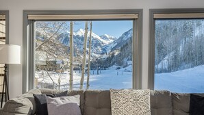 Un salon doté d’une grande fenêtre donnant sur un paysage de montagnes enneigées et d’un village.