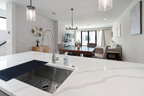 Une cuisine moderne dotée d’un îlot central, d’un évier en acier inoxydable et de luminaires suspendus.