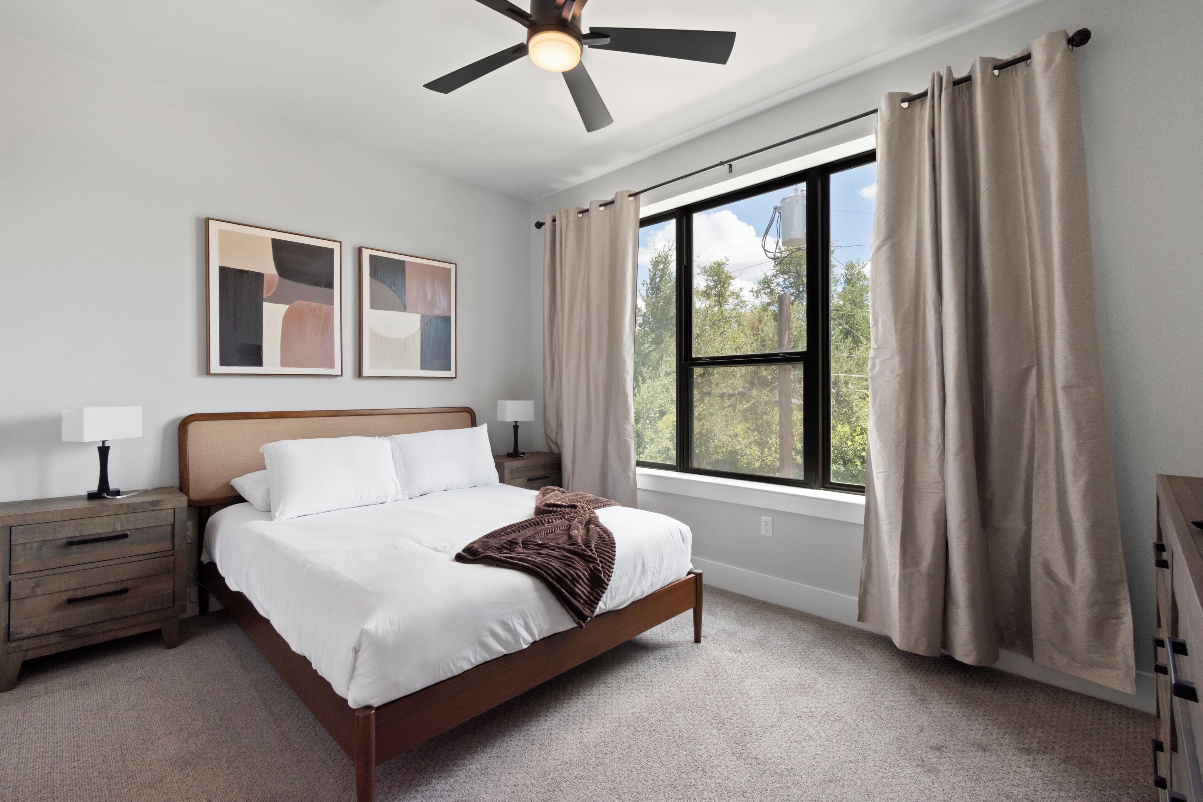 A bedroom with a bed, nightstands, a ceiling fan, and a large window with curtains.