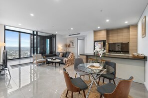 Een moderne woonkamer met een groot raam, een eethoek en een keuken met houten kastjes.