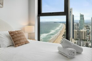 Een hotelkamer met een bed, een kussen, een lamp en uitzicht op de oceaan en de stadshemel.