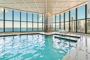 Ein Hallenbad mit klarem, blauem Wasser, großen Fenstern mit Blick auf den Ozean und die Stadtlandschaft sowie einem modernen architektonischen Design.
