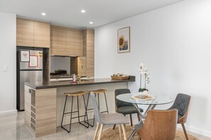 Une cuisine moderne avec un îlot central, des tabourets de bar, une table de salle à manger ronde et un tableau encadré au mur.