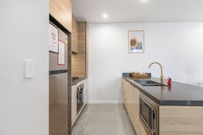 A modern kitchen with stainless steel appliances, a black countertop, and a wooden cabinet. - Ocean Luxe Retreat 2  Kingbeds Free Parking (Surfers Paradise)