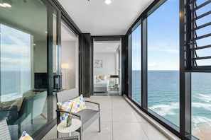 Ein Balkon mit Meerblick, eine Sitzecke mit Tisch und ein Schlafzimmer mit Bett und Nachttisch.