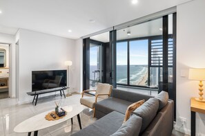 A modern living room with a flat-screen TV, a sofa, a coffee table, and a view of the ocean. - Ocean Luxe Retreat 2  Kingbeds Free Parking (Surfers Paradise)