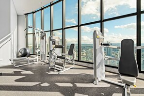 Une salle de sport équipée de matériel d’exercice et dotée de grandes fenêtres donnant sur la ville.