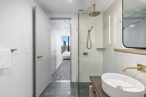 Ein modernes Badezimmer mit einer Duschkabine aus Glas, einem weißen Waschbecken und Blick auf eine Stadtkulisse durch die Tür.