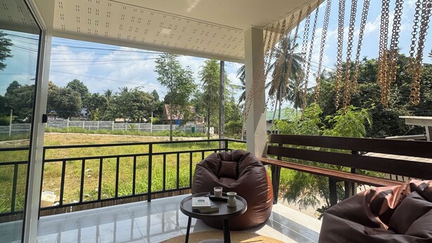 A balcony with a bean bag chair, a small table with a book and a cup, and a view of a green field and trees. - Boho House • 2 mn DeviDeli • Hin Kong • 4K Tv • AC (Koh Phangan)