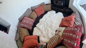 A cozy seating area with a fireplace, surrounded by various cushions and a furry rug.
