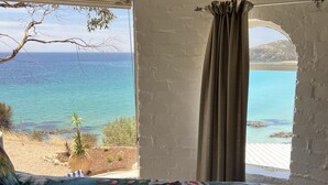 A room with a bed featuring a floral-patterned bedspread, a view of the sea, and a window with curtains.