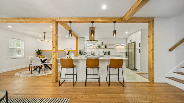 A modern kitchen with wooden beams, a central island with bar stools, and a dining area with a striped rug. - Modern Rustic Retreat - Cozy 4-Bedroom ATL (Decatur)