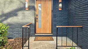 A modern house entrance with a wooden door, black brick walls, and a metal gate. - Modern Rustic Retreat - Cozy 4-Bedroom ATL (Decatur)