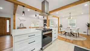 A modern kitchen with white cabinetry, a stainless steel range hood, and pendant lighting. - Modern Rustic Retreat - Cozy 4-Bedroom ATL (Decatur)