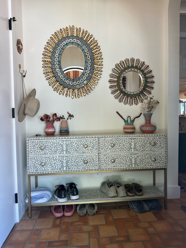 A hallway with a decorative mirror, a wall-mounted hat rack, a patterned dresser, and a shoe rack.