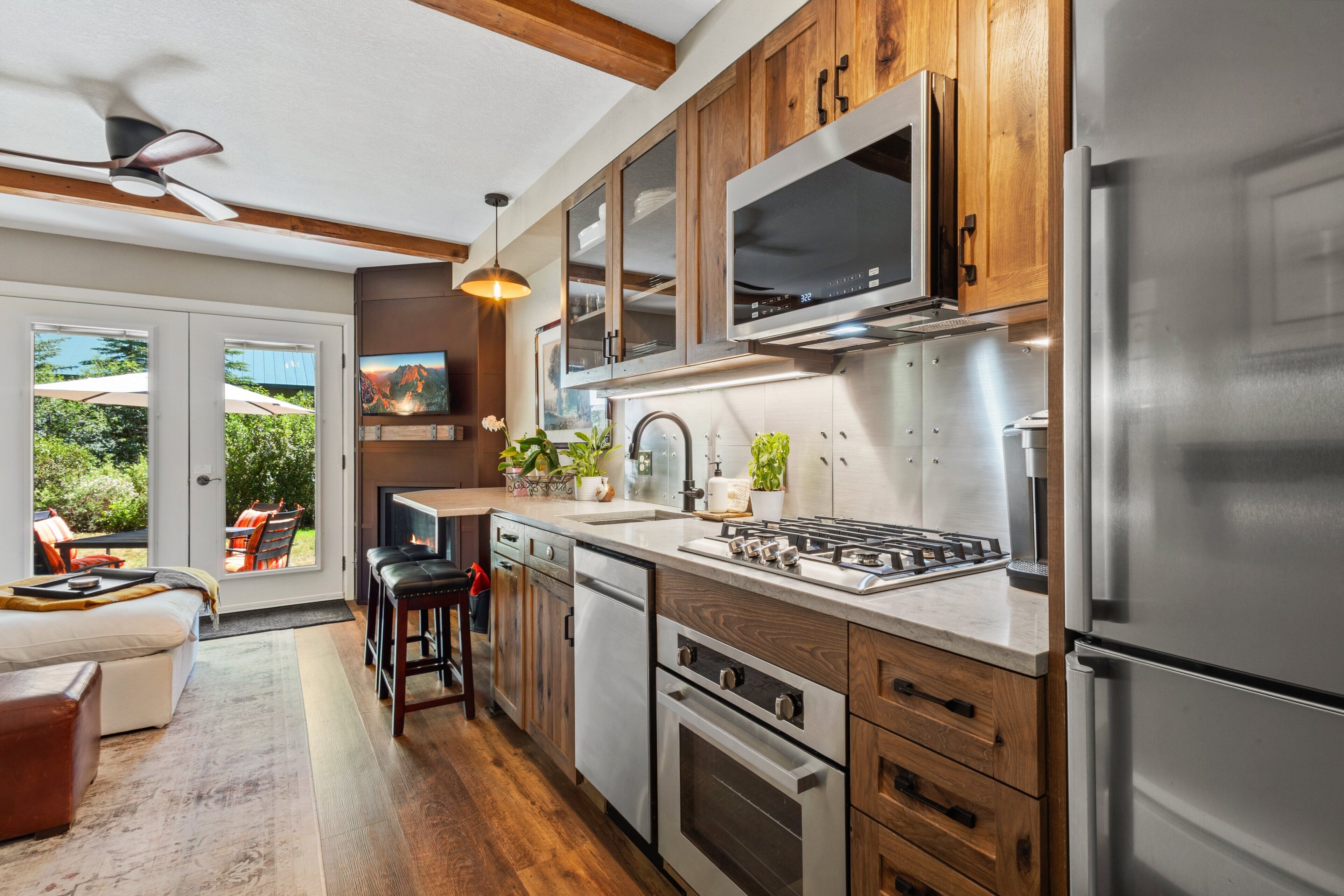 A modern kitchen with stainless steel appliances, wooden cabinets, and a large window overlooking a garden.