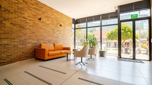 A lobby with a brick wall, orange sofa, two chairs, a coffee table, and large windows with a view of the street. - Loft with unique view of the Center and Monserrate (Bogotá)
