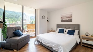 A modern bedroom with a large bed, a gray sofa, and a view of the city and mountains through large windows. - Loft with unique view of the Center and Monserrate (Bogotá)