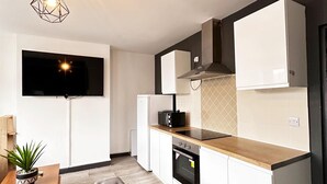 A modern kitchen with a flat-screen TV, a built-in oven, and a dining area with a wooden table and a potted plant. - Willow Suite - 3br - Sleeps 8 - Central Blackpool (Blackpool)