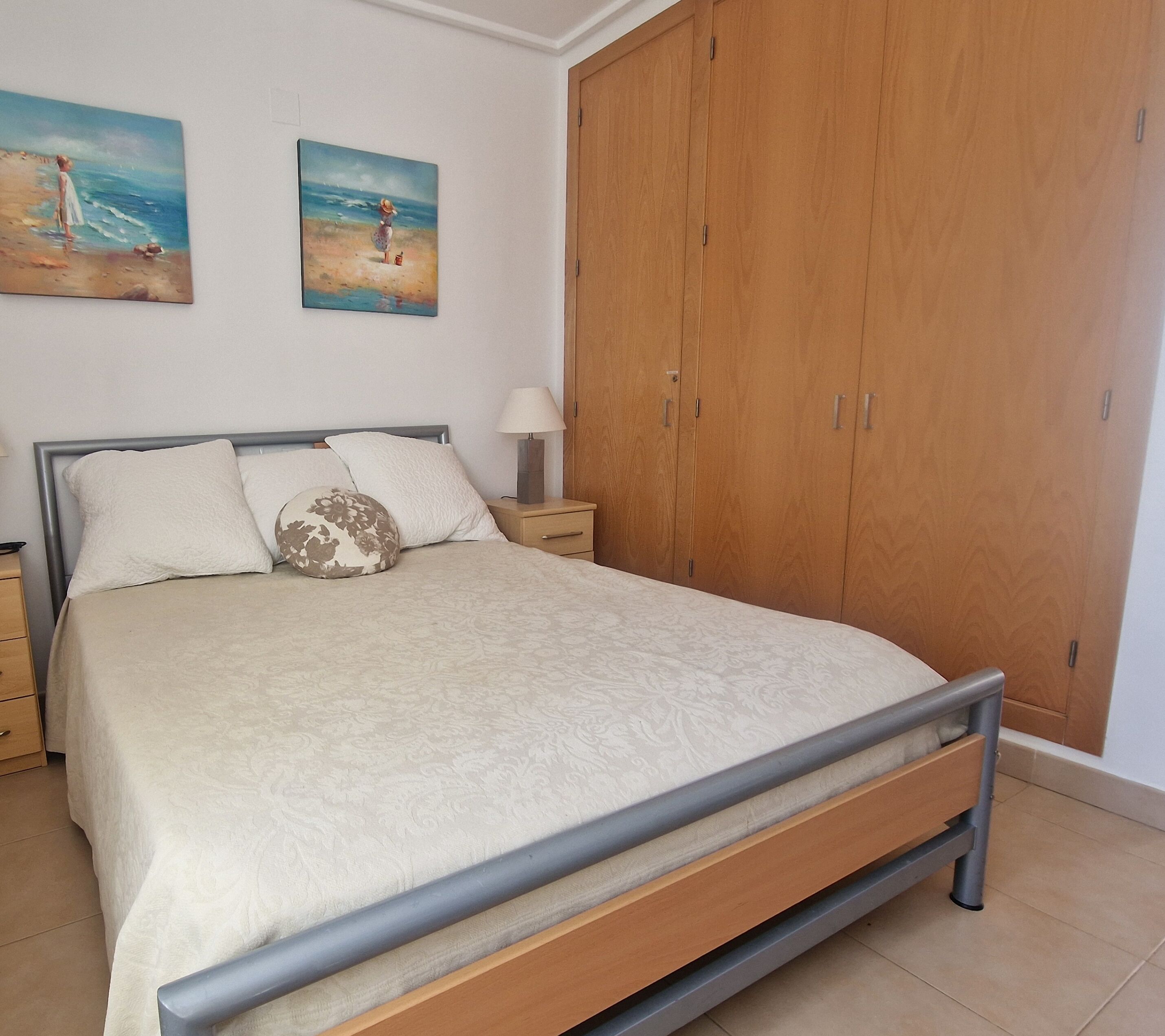 Ein Schlafzimmer mit einem Bett, einem Nachttisch, einem Holzschrank und zwei Wandbildern.