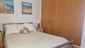 A bedroom with a bed, a nightstand, a wooden wardrobe, and two wall paintings.