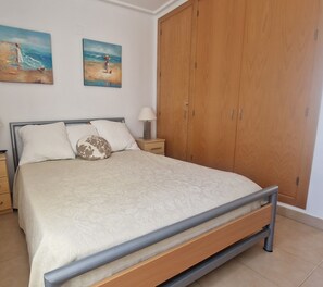 Quarto com cama, mesa de cabeceira, guarda-roupa de madeira e dois quadros na parede.