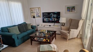 A living room with a teal sofa, a beige armchair, a coffee table, a TV, and a lamp.