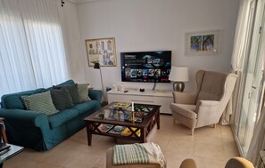 Uma sala de estar com um sofá azul-esverdeado, uma poltrona bege, uma mesa de centro, uma televisão e um abajur.