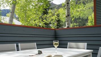 Una terraza de madera con una mesa, sillas, una copa de vino y un libro abierto.