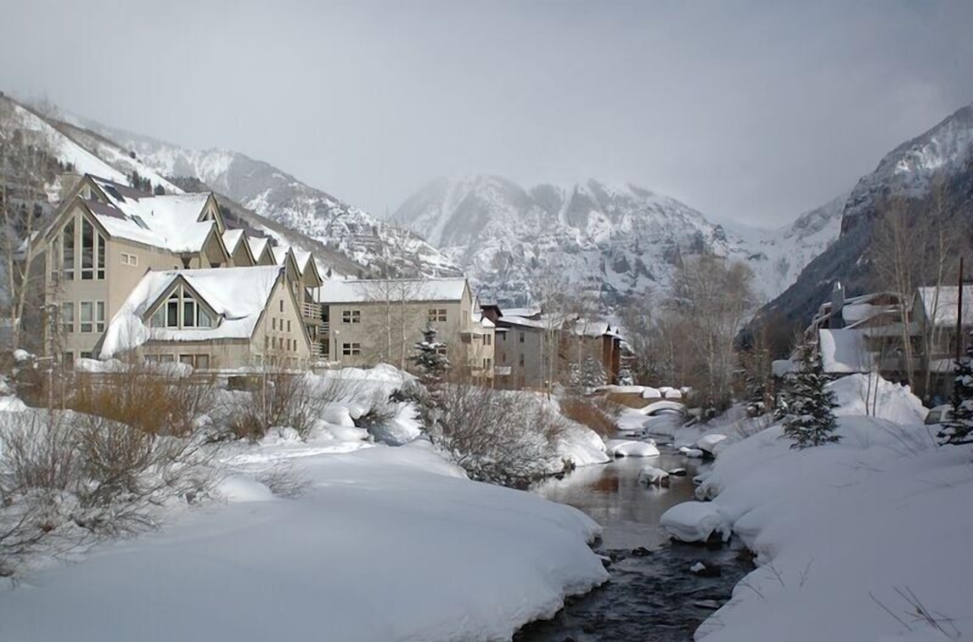 A snow-covered mountain town with buildings along a river.