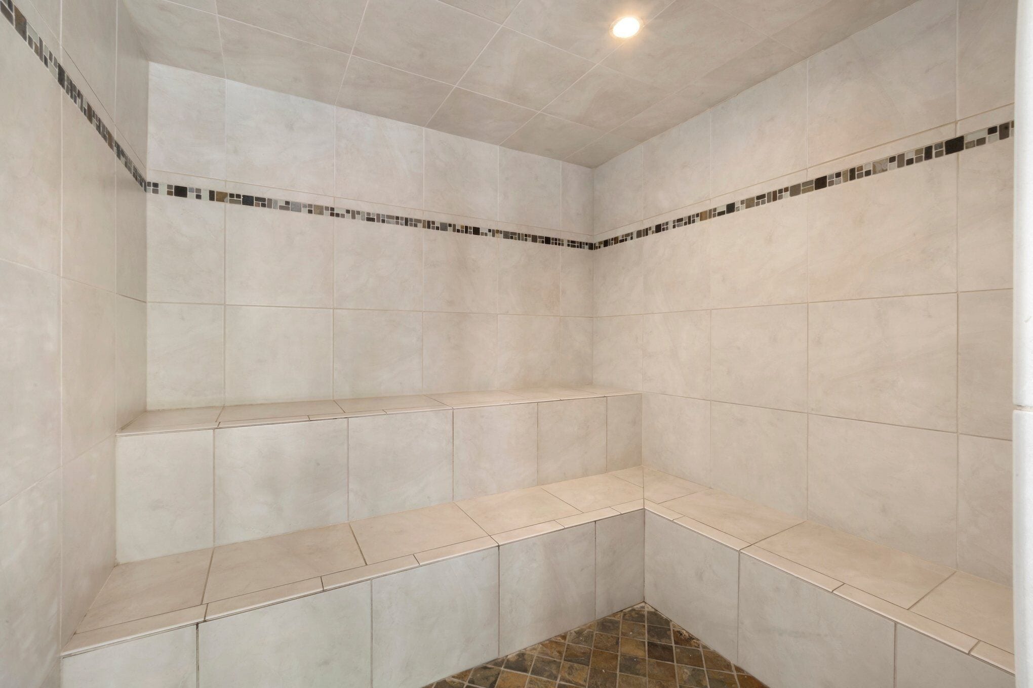 A bathroom with beige tiles, a tiled bench, and a small tiled area at the bottom.