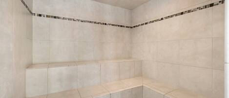A bathroom with beige tiles, a tiled bench, and a small tiled area at the bottom.