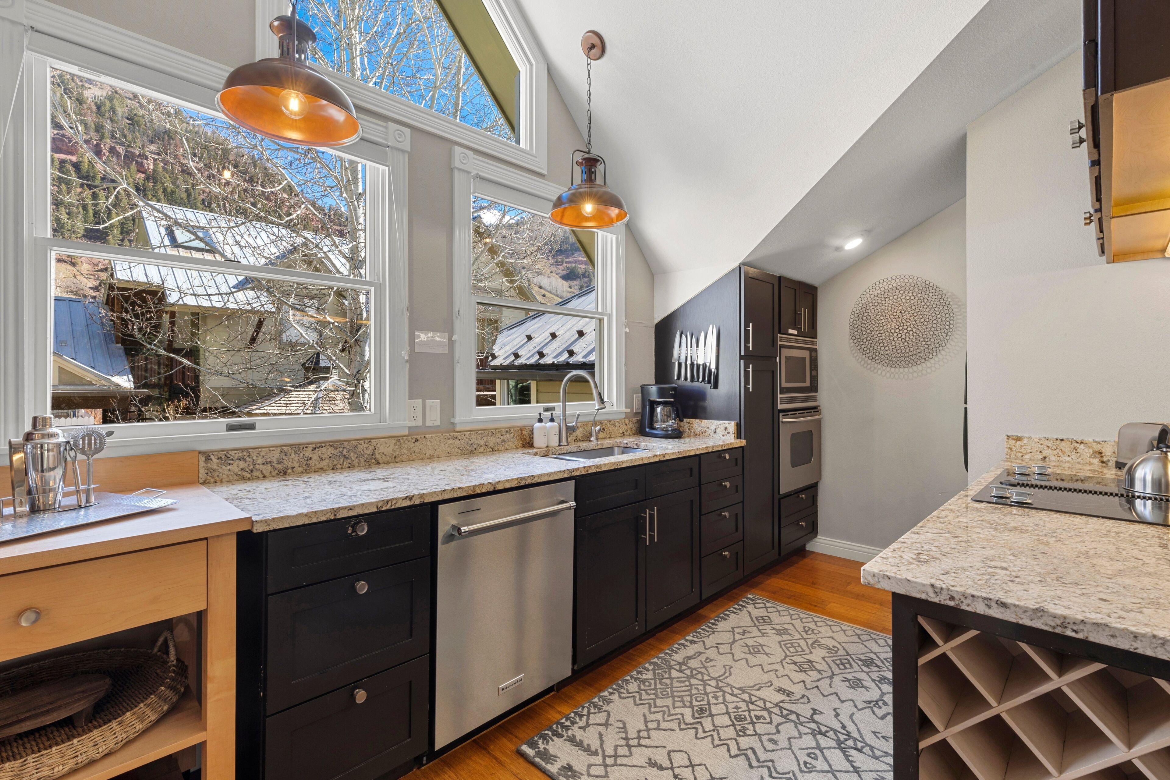 A modern kitchen with a dishwasher, stainless steel appliances, and a large window offering a view of a mountainous landscape.