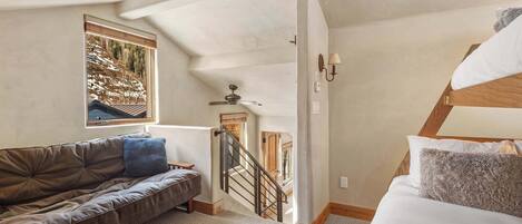 Un dormitorio con una cama litera, un sofá, una ventana con vistas, una escalera y un ventilador de techo.