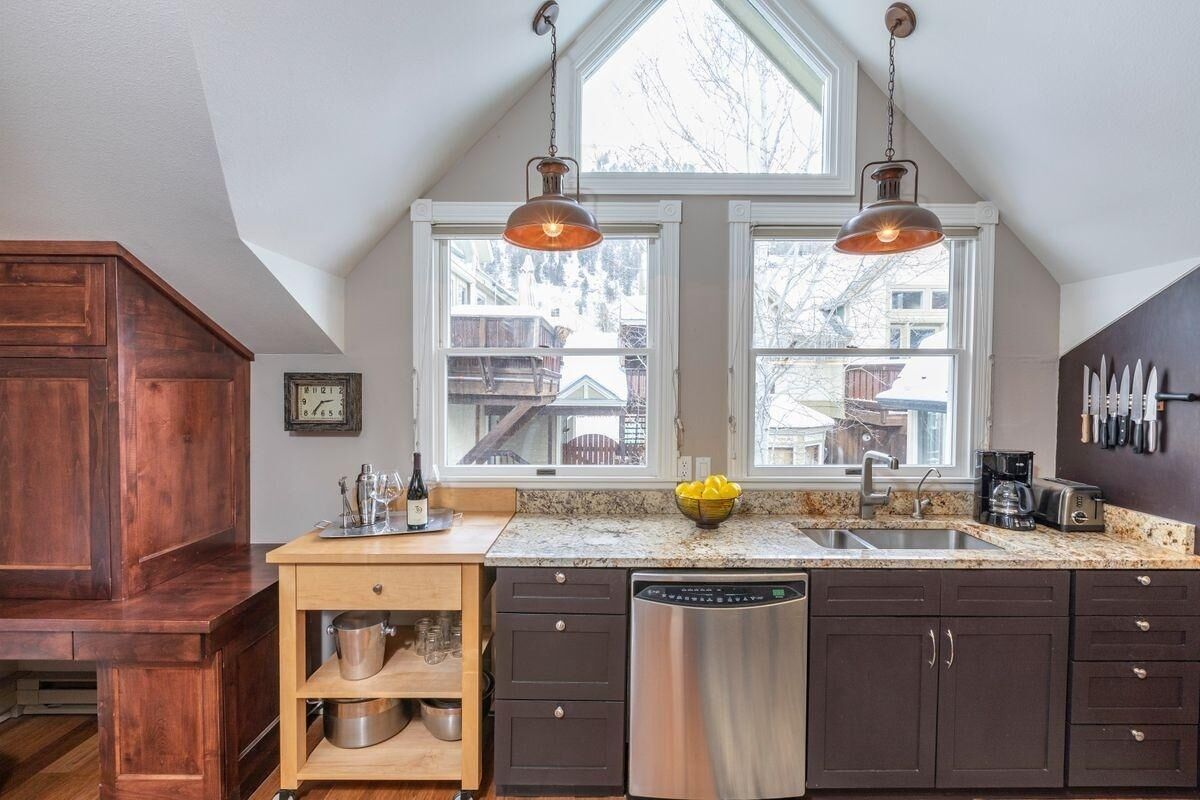 A kitchen with a wooden cabinet, a dishwasher, a sink, and a window with a view of a house.