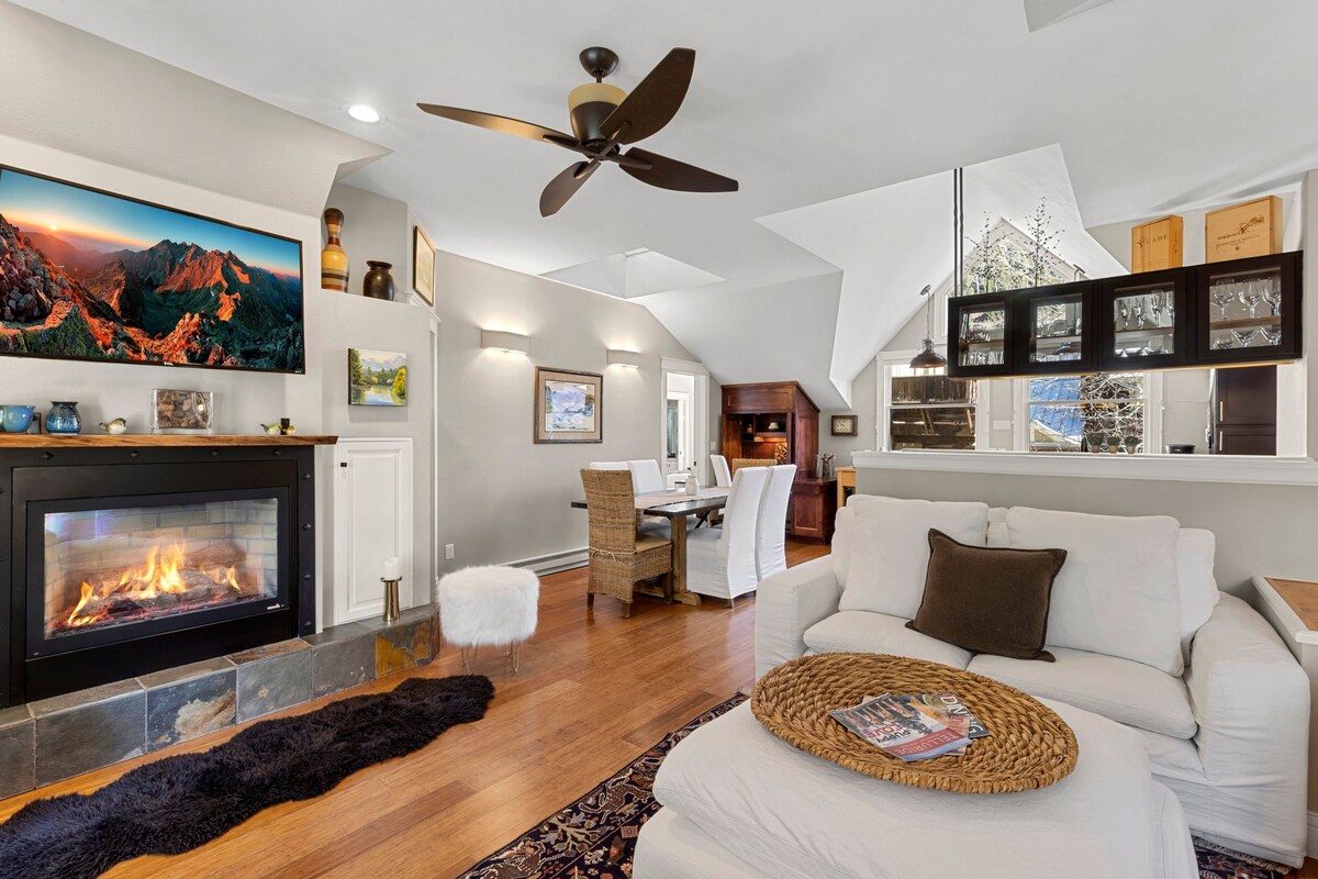 A modern living room with a fireplace, a ceiling fan, and a dining area.