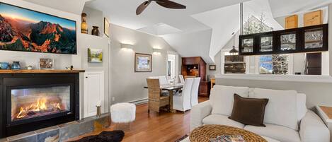 A modern living room with a fireplace, a ceiling fan, and a dining area.