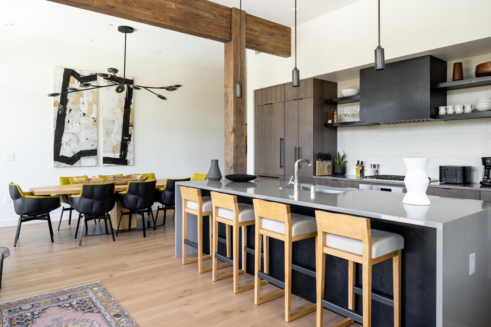 A modern kitchen with a central island, bar stools, and a dining area with a table and chairs.