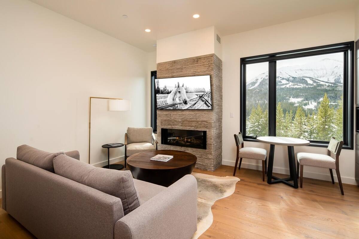 Ein modernes Wohnzimmer mit Kamin aus Stein, einem großen darüber hängenden Fernseher, einer gemütlichen Couch, einem Couchtisch und einem Essbereich mit Stühlen.