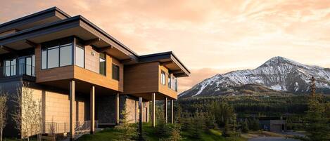 Una casa moderna de dos pisos con ventanas amplias y un paisaje de montañas al fondo.