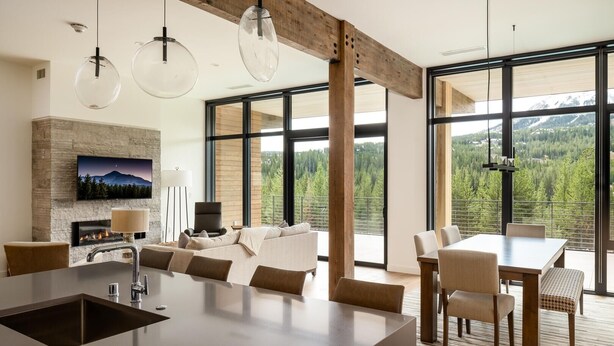 Una cocina moderna con una isla central, comedor con mesa y sillas, chimenea y amplios ventanales con vistas a la montaña.