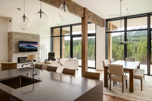 A modern kitchen with a central island, dining area with a table and chairs, a fireplace, and large windows offering a mountain view. - Big Sky Lake Lodge (Big Sky)