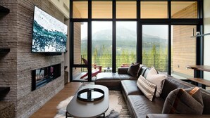 Una sala de estar moderna con chimenea, ventanas grandes y vistas a las montañas.