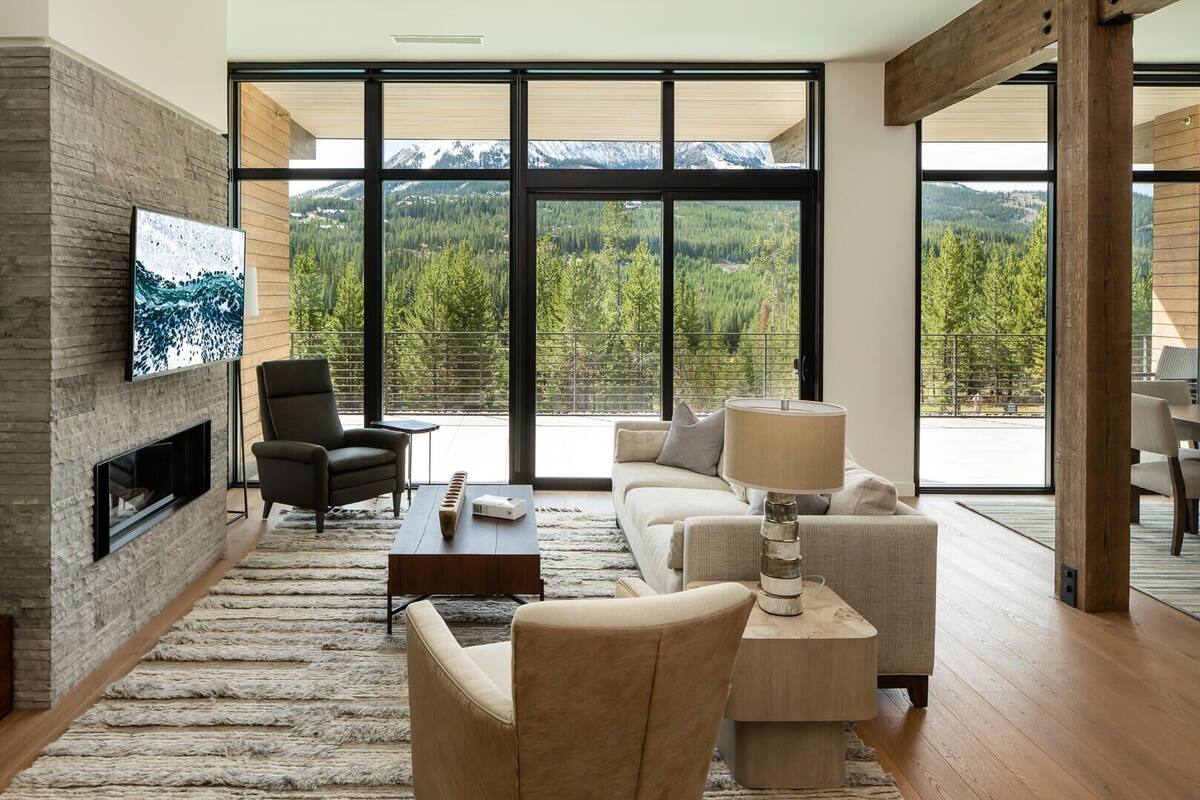 Ein modernes Wohnzimmer mit Kamin, bequemen Sitzgelegenheiten, einem großen Fernseher und Blick auf eine Berglandschaft.
